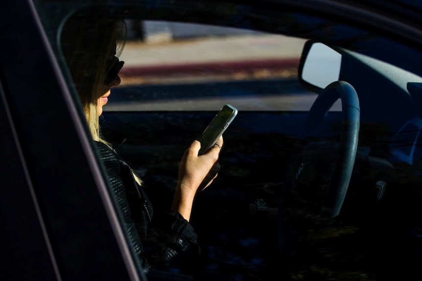 A side shot through a car window of a woman looking at her mobile phone while in the driver's seat.