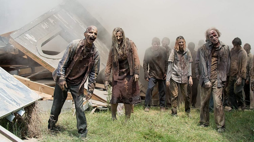 A group of zombies walking forward among destroyed buildings