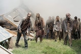 A group of zombies walking forward among destroyed buildings