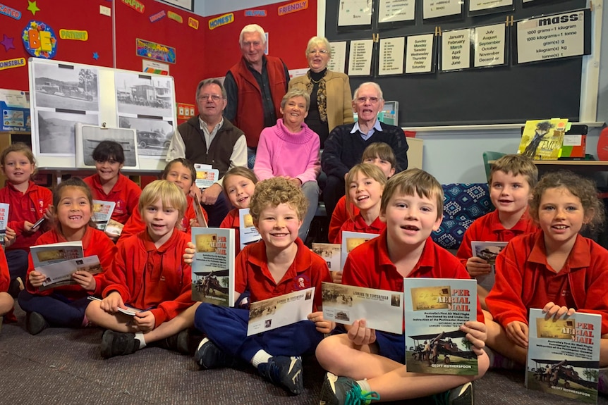 Children sit on a classroom floor holding a book on air mail history and an Australia Post commemorative envelope.