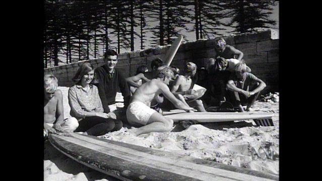 Old photo shows teenagers sitting on beach with surfboard