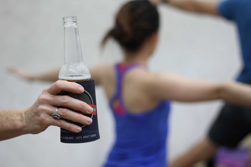 A beer bottle in the foreground with a background of a woman doing yoga
