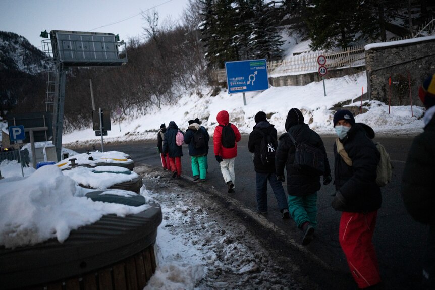Migrants walk along mountain road.