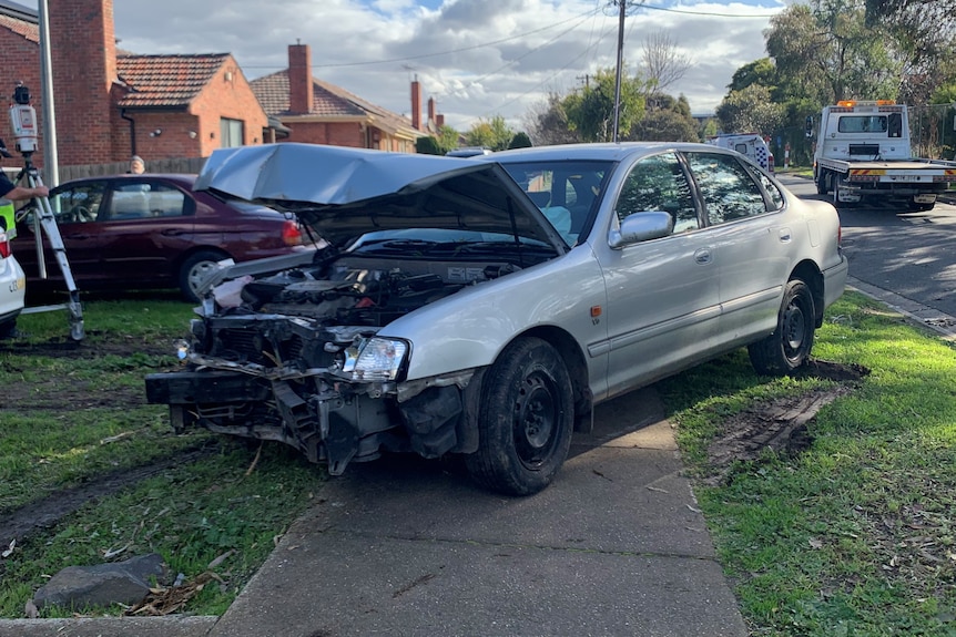 the car in the front garden of a home. The front of the car is badly damaged, the bumper is missing.