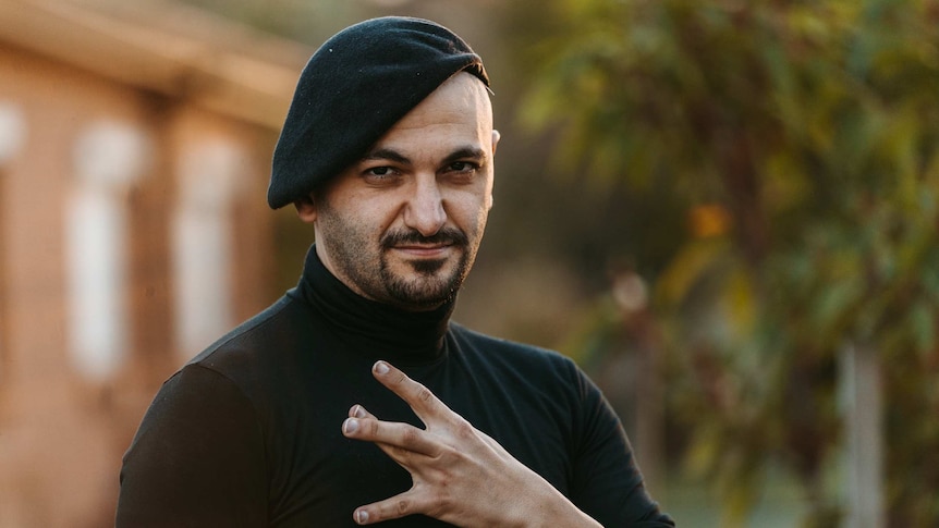 The Lebs book author Michael Mohammed Ahmad poses for a portrait wearing a black skivvy and beret doing a westside gang sign.