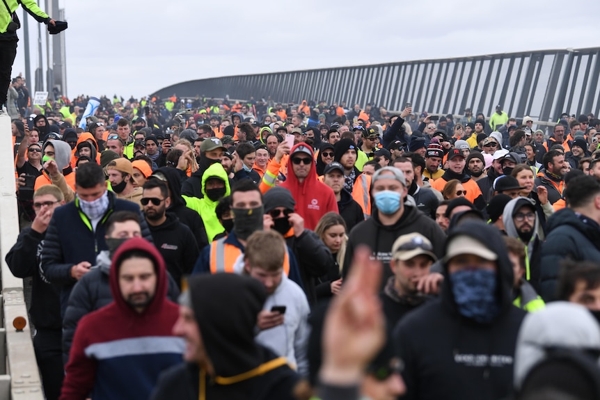 Protesters fill several lanes of the freeway on the West Gate Bridge under grey skies.