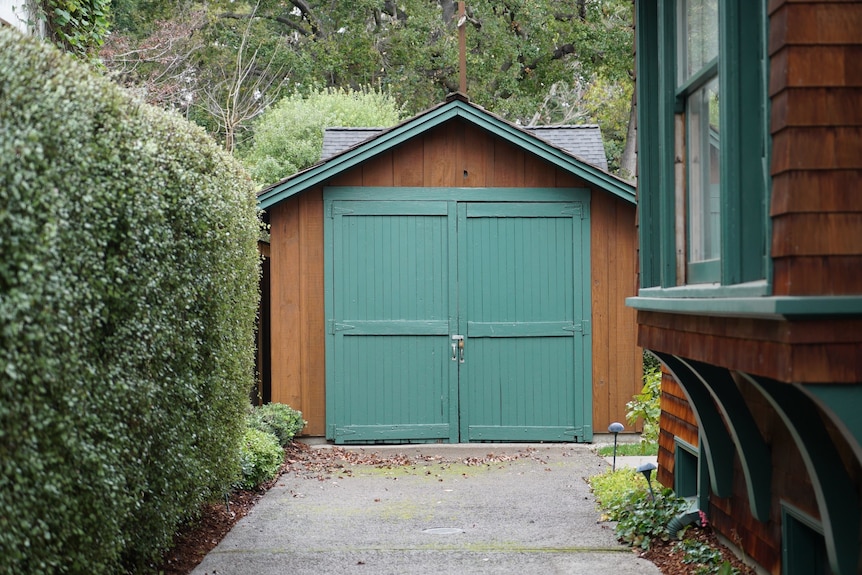 A garage, with brown wood and a green door, at the end of a driveway.