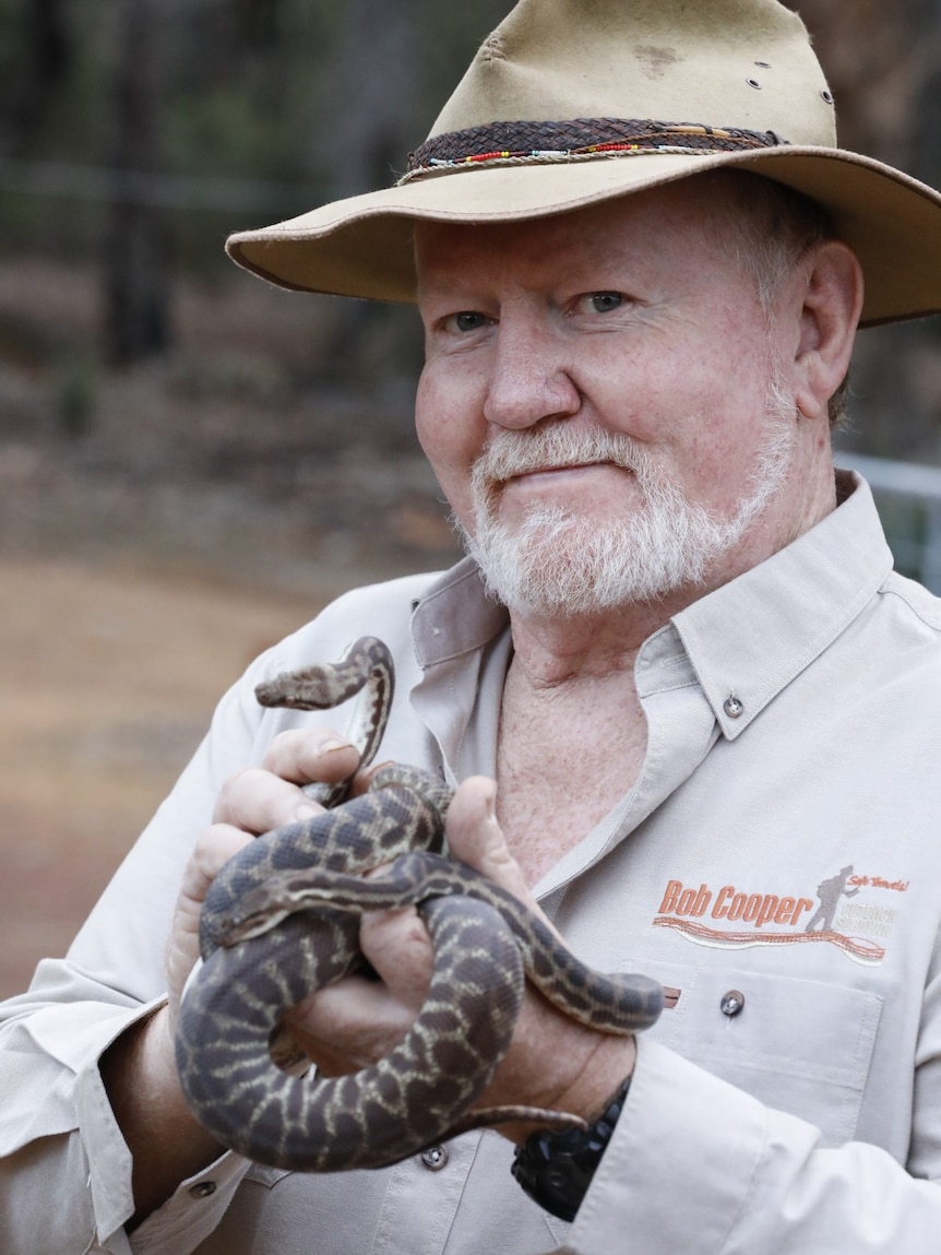 A man in a broad-brimmed hat holding a snake.