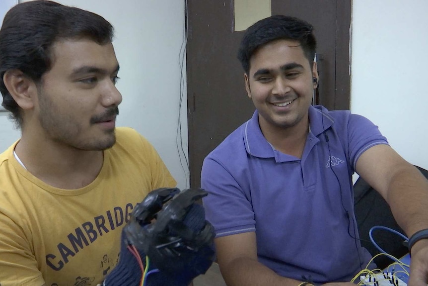 Mechatronics students Narendra Kandori and Subhankar Singh smile and tinker with a robotic hand.