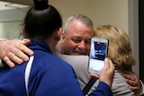 two women hug ricky davis as one of the women holds up an iphone