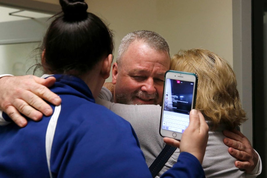 two women hug ricky davis as one of the women holds up an iphone