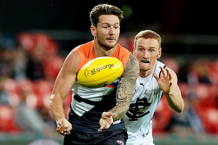 A GWS Giants AFL player handballs in front of a Carlton opponent.
