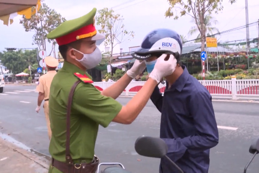 A Vietnamese police officer puts a mask on a motorbike commuter in April 2020.
