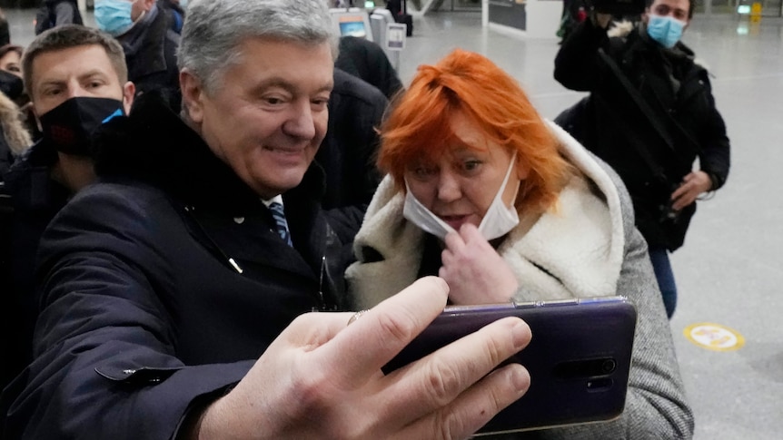 Man stands next to woman holding phone in selfie mode for photo