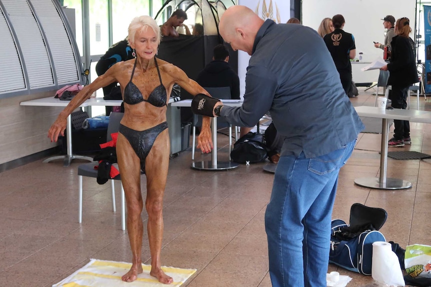 Janice Lorraine's partner David Kendall pats fake tan on to her before the competition.