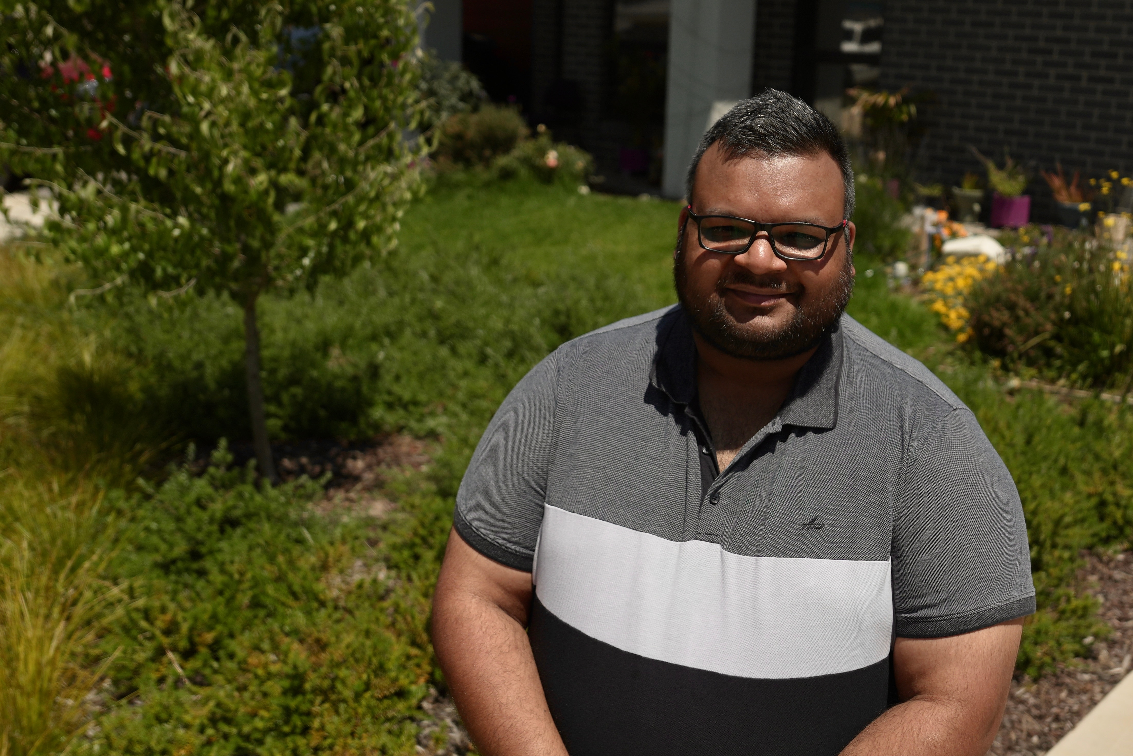 Rupain Saini sorrindo em seu jardim cercado por um jardim verdejante.