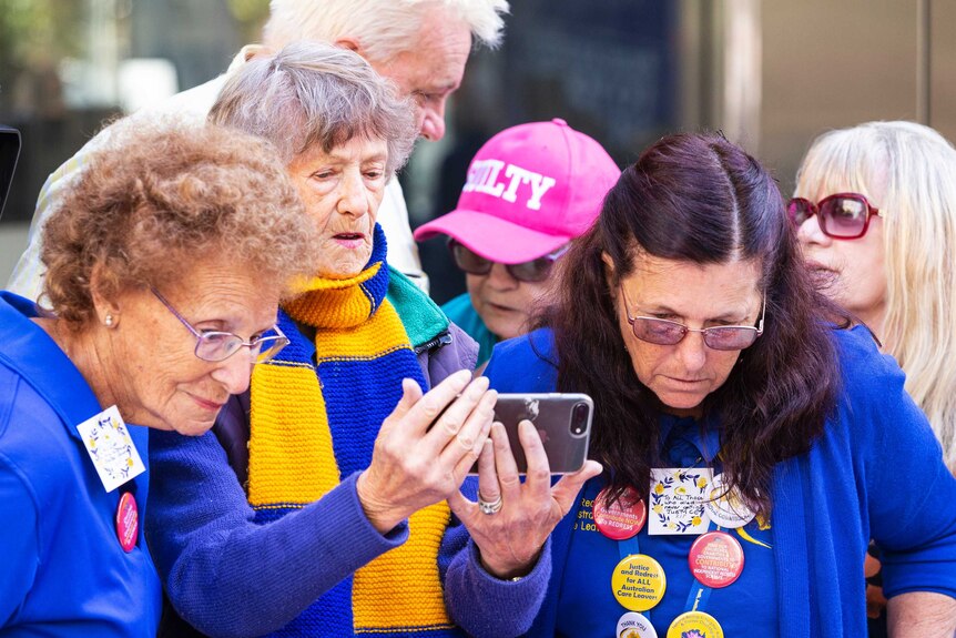Several mature women gather around one women holding a mobile phone.