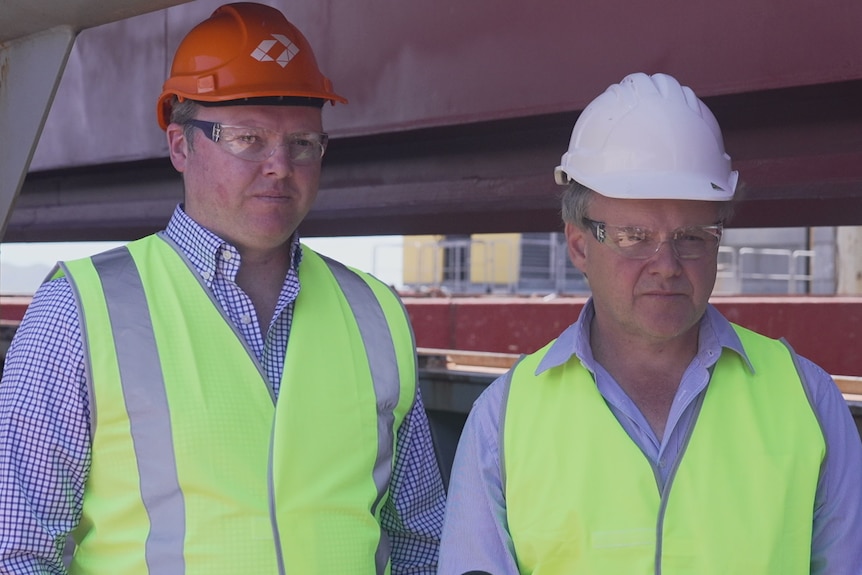 Two men wearing hard hats, high-vis and safety glasses.