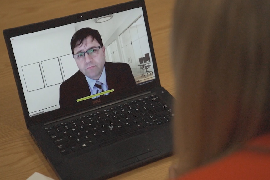 A man wearing glasses and a suit and tie appears on a laptop screen.