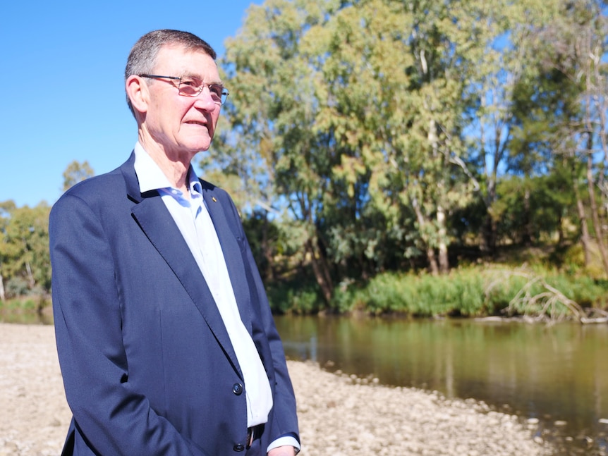 Man in suit looks out at river.