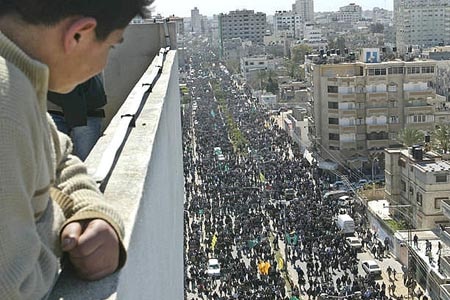 A young boy on a balcony looks down onto a street filled with people.