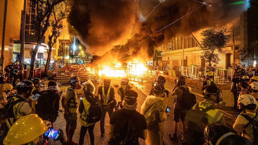 Journalists and photographers stand around in protective gear as a fire rages in terraces during a protest