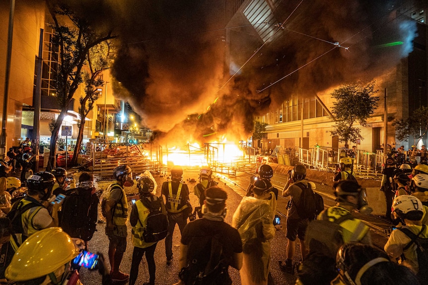 Journalists and photographers stand around in protective gear as a fire rages in terraces during a protest