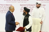 A Taliban wearing a turban and traditional dress shakes hands with a US representatives wearing a suit.
