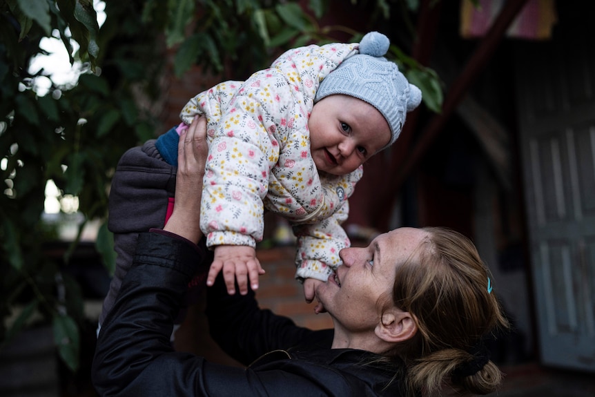 A woman lifts a baby into the air. 