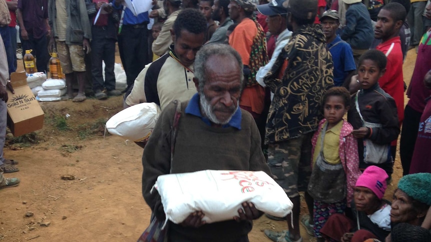 Papua New Guineans walk with aid packages