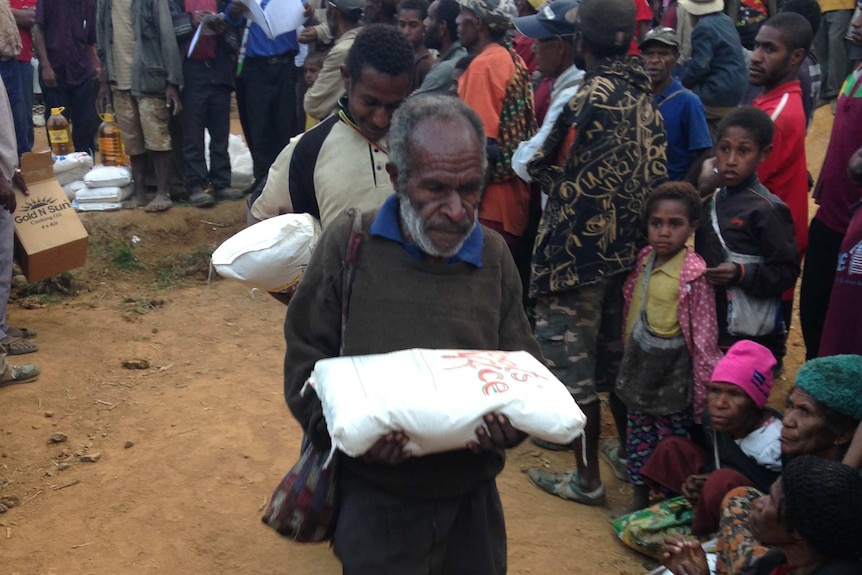 Papua New Guineans walk with aid packages
