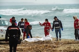 Italian Red Cross volunteers and coast guards recover a body after a migrant boat broke apart in rough seas, at a beach.