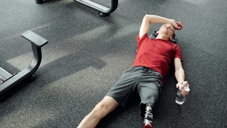 A man lying on the floor of a gym looking exhausted.