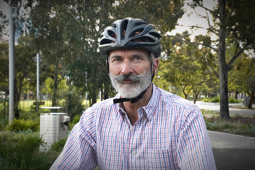 A man with a grey beard and helmet on sits on a bike