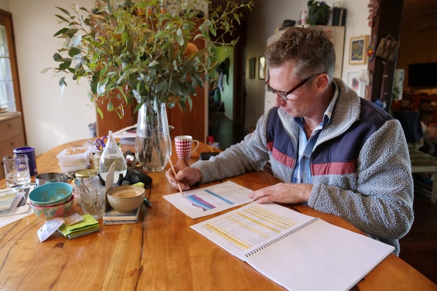Man sits at kitchen table with pencil and calculations 