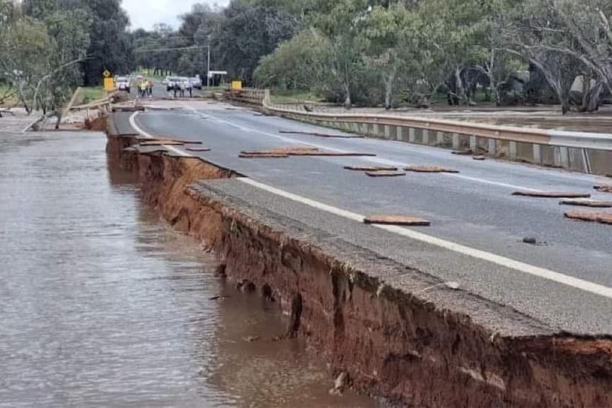 side of a road falls away, surrounded by floodwaters