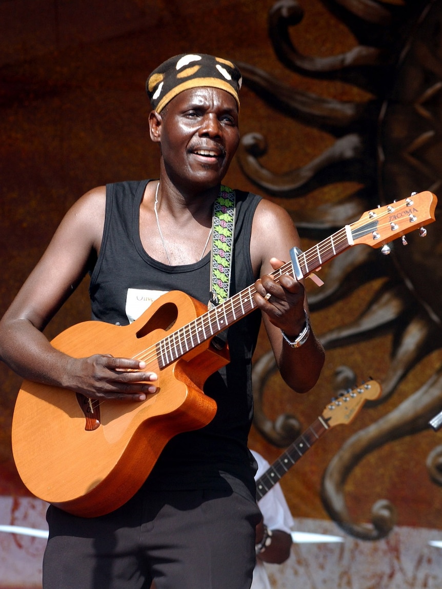 A musician in a singlet plays a guitar on stage.