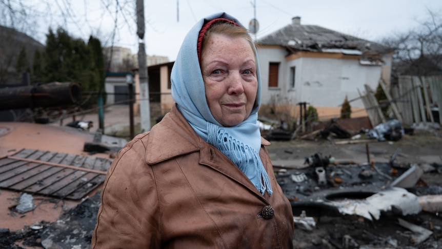 A woman wearing a blue scarf around her head and brown jacket cries.