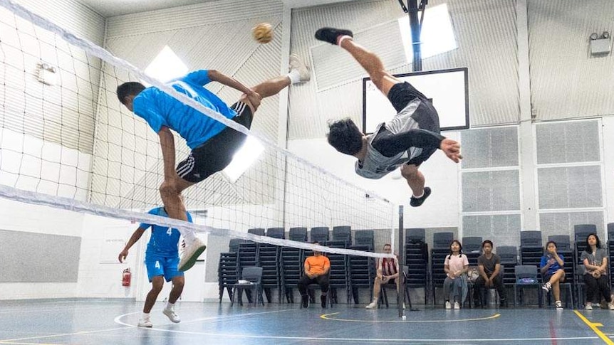 A man flies upside down kicking a small ball over a net.