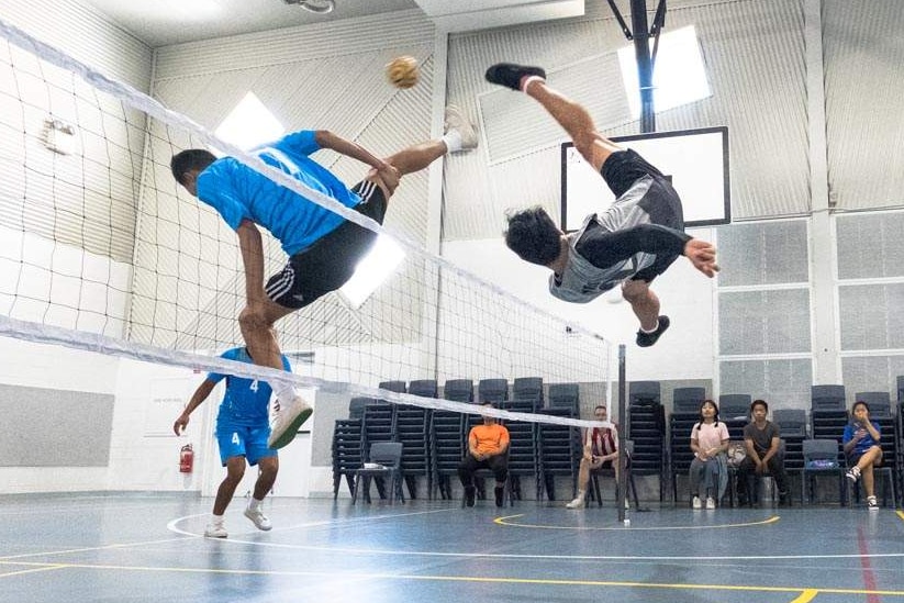 A man flies upside down kicking a small ball over a net.