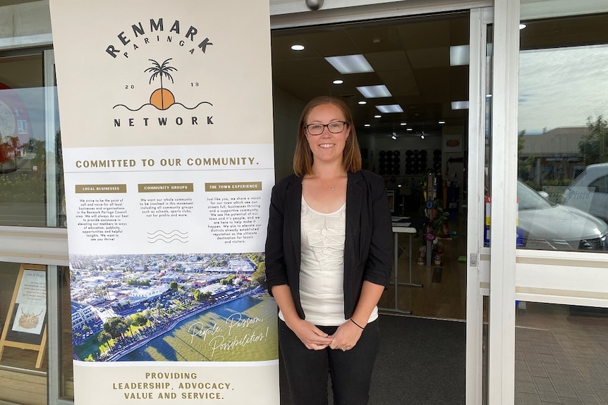 A woman is standing next to a sign smiling. She is wearing a black blazer and white shirt. The sign says Renmark Paringa Network