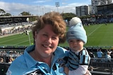 Lyn Gannon smiles with granddaughter Zara on her hip. She wears a Sharks jersey, and the toddler wears a beanie and top.