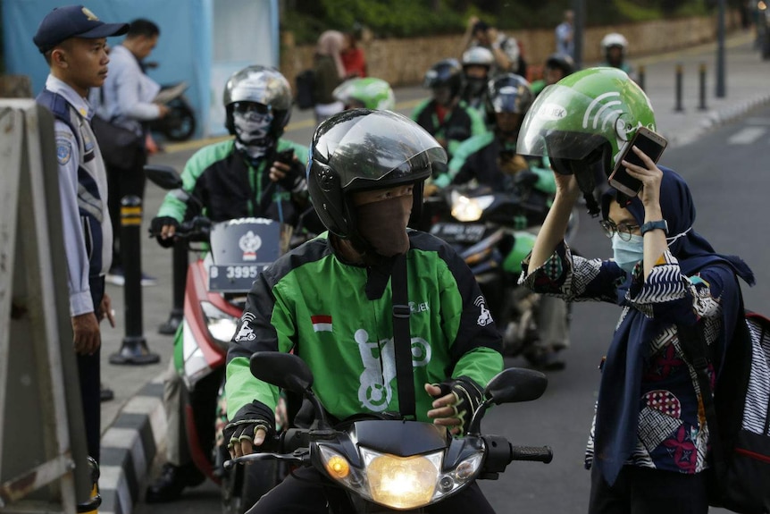 Rows of motorcyclists in helmets line up at a Jakarta stopping.