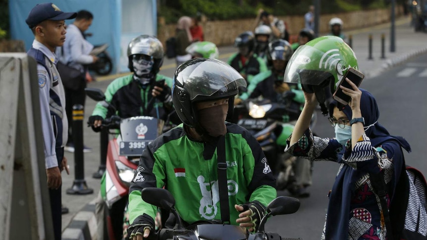 Rows of motorcyclists in helmets line up at a Jakarta stopping.