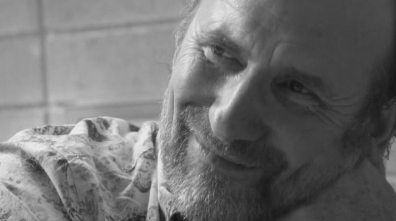 Colin Hay with head in hands, smiling. Black and white image.