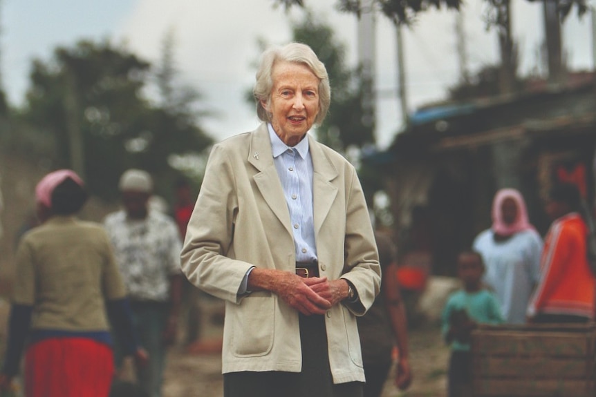 A woman standing in a busy unpaved street clasps her hands