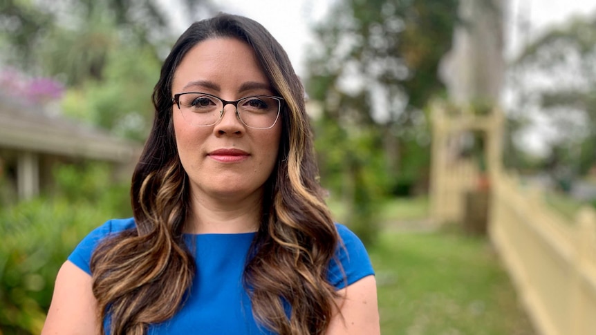 A woman with glasses and a blue top looking at camera, arms folded