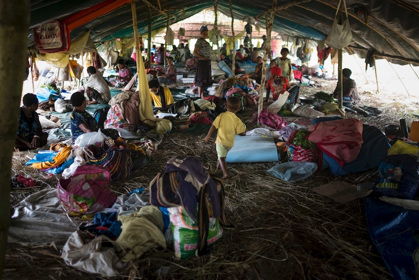 Wide shot of a group of people sitting inside a large makeshift tent.