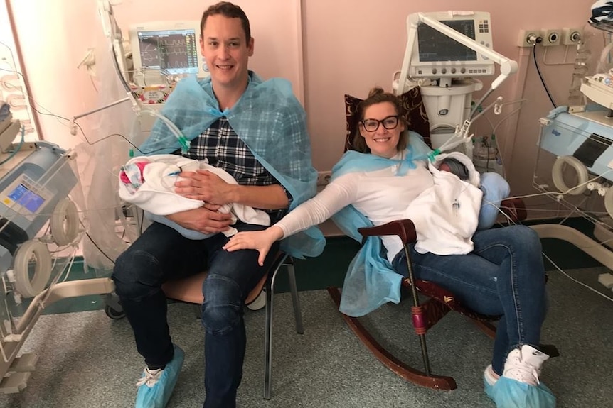 Dale and Louise Pitcher each hold one of their new-born twins, sitting in chairs in the hospital room in Ukraine