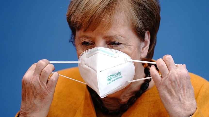 A woman stretches the elastic on a disposable mask as she puts it on